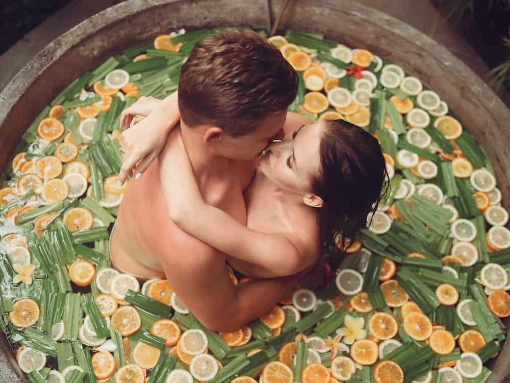 A Naked Heterosexual Couple Getting Intimate in a Wooden Bath Filled with Citrus Fruit and Leafy Greens