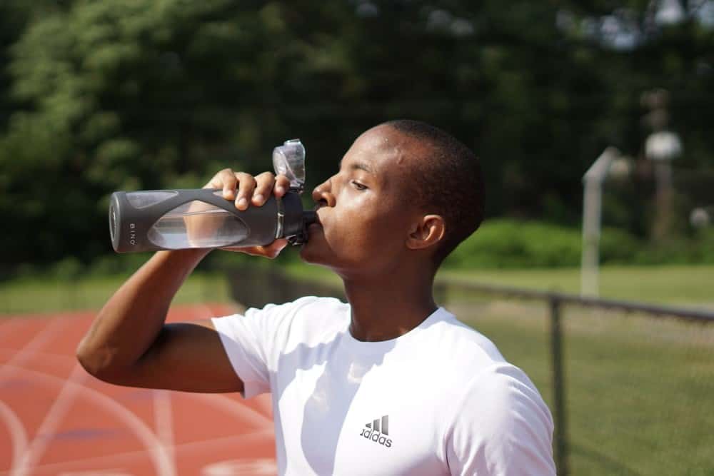 A Man in a White T-Shirt Drinking from a Water Bottle