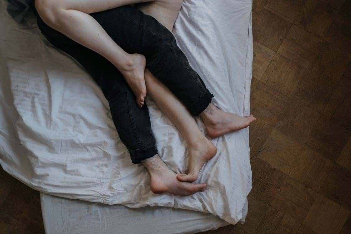 Two Pairs of Legs—One Male and One Female—Tangled in Bed