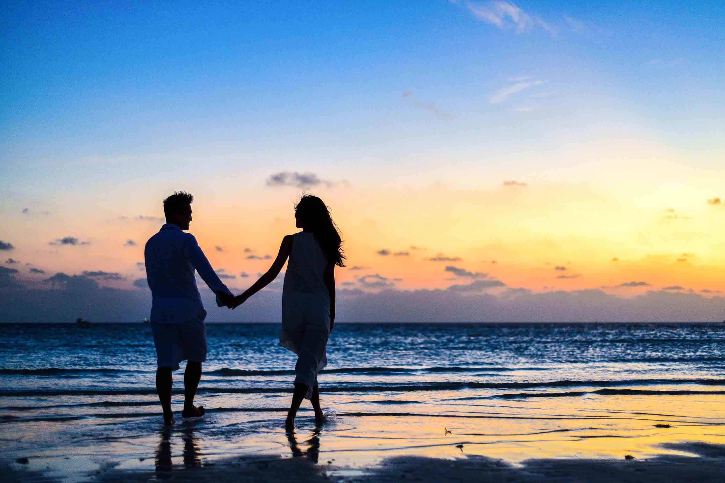 man and woman holding hands on the beach